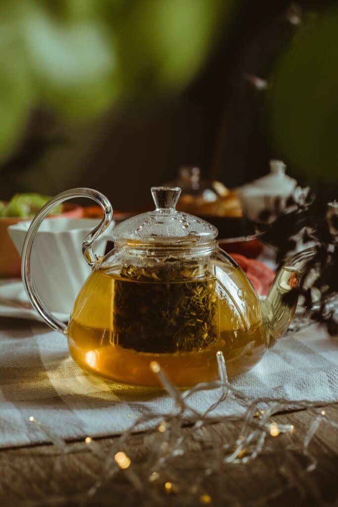 A stylish glass teapot filled with herbal tea on a cozy table setting with soft lighting.