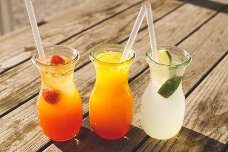 Close-up of three refreshing beverages with citrus, strawberries, and lime on a sunny wooden table.