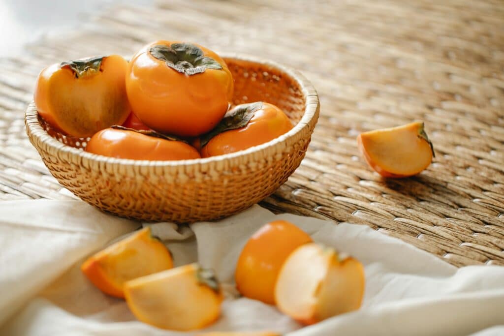 A wicker basket filled with ripe persimmons on a textured surface, symbolizing natural and healthy eating.