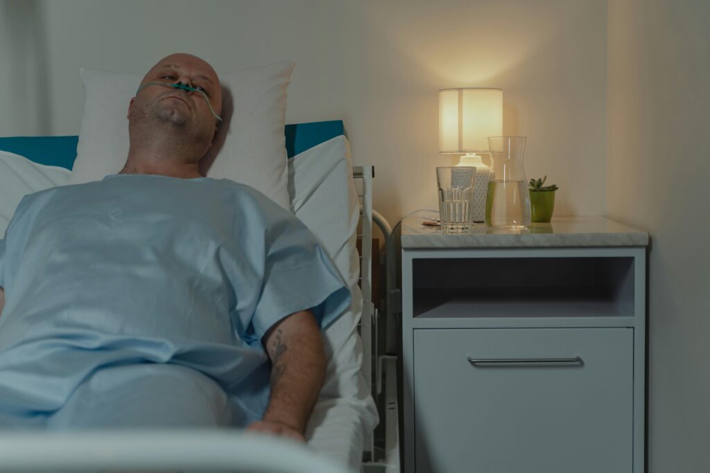 A man lying in a hospital bed with a nasal cannula, illuminated by bedside lamp.