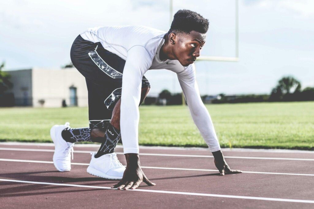 Focused athlete in starting position on a sunny track field, ready to sprint.