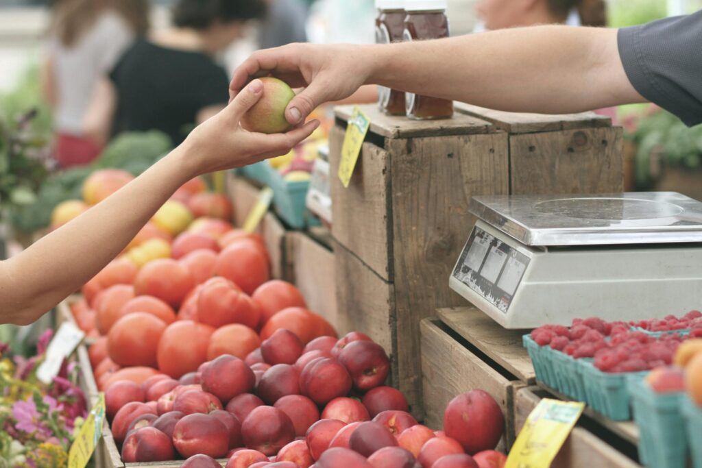 A customer exchanges an apple with a vendor at a vibrant farmers market.