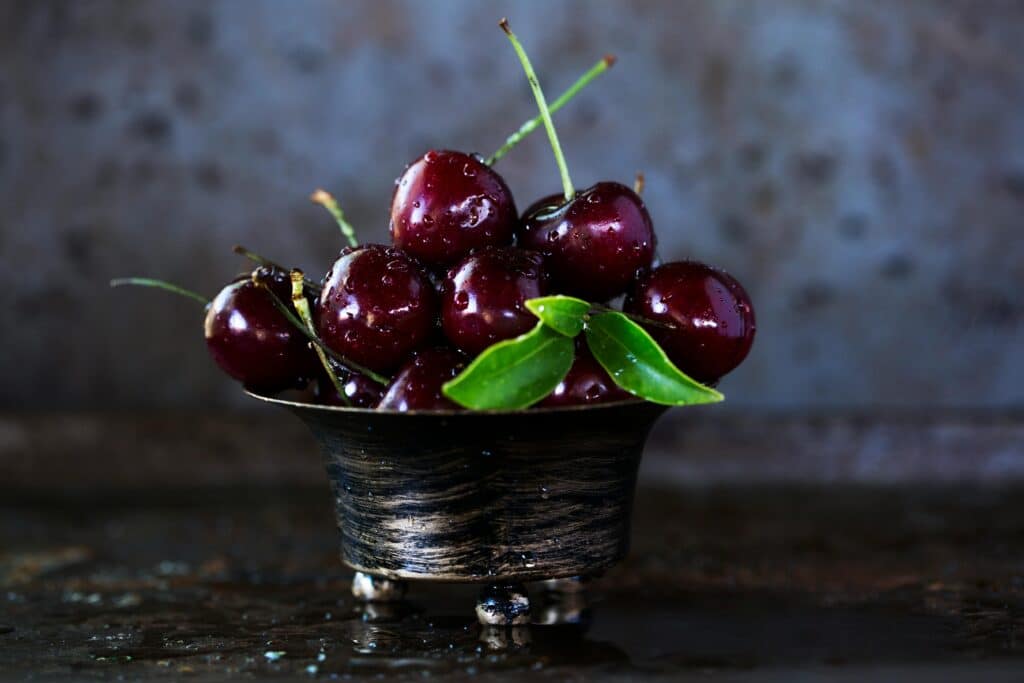 A rustic metal bowl filled with fresh, juicy cherries glistening with moisture.