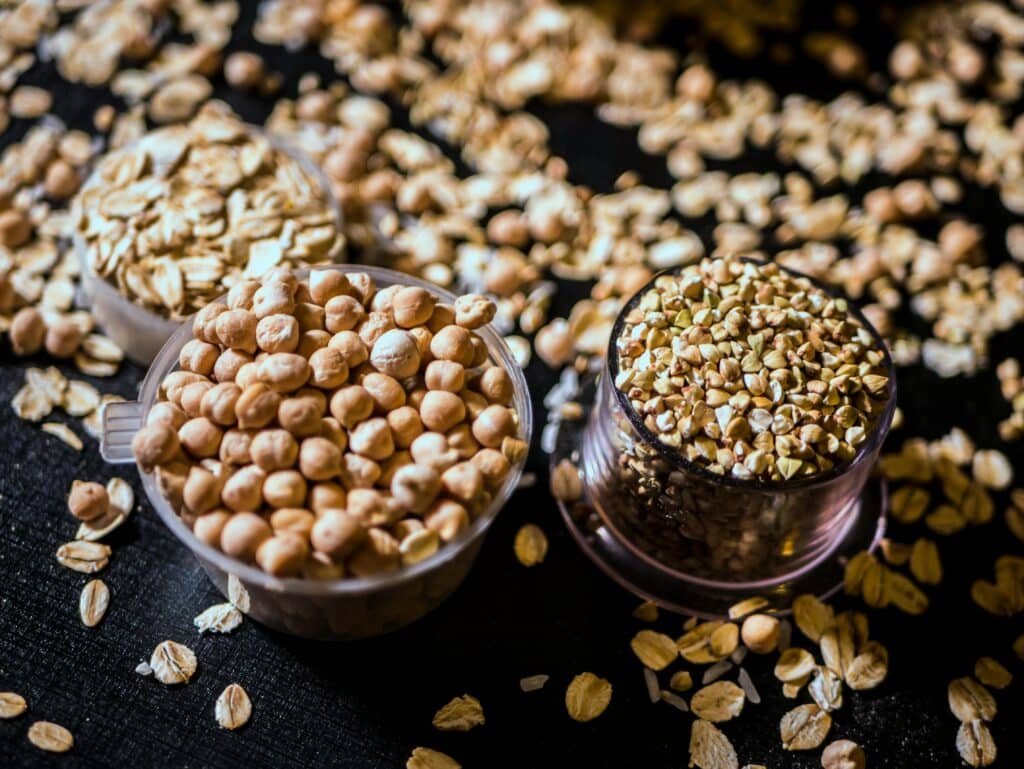 Close-up of assorted raw grains and seeds in cups on a dark background, showcasing variety and texture.