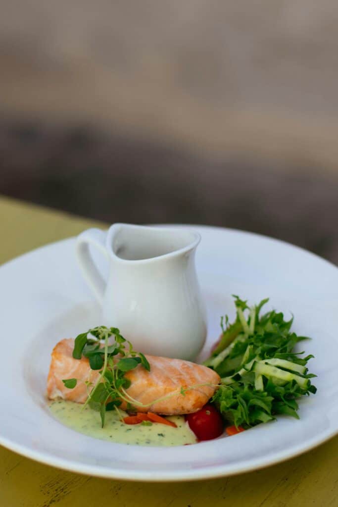 Gourmet salmon dish with greens and sauce on a white plate, enticing meal photo.