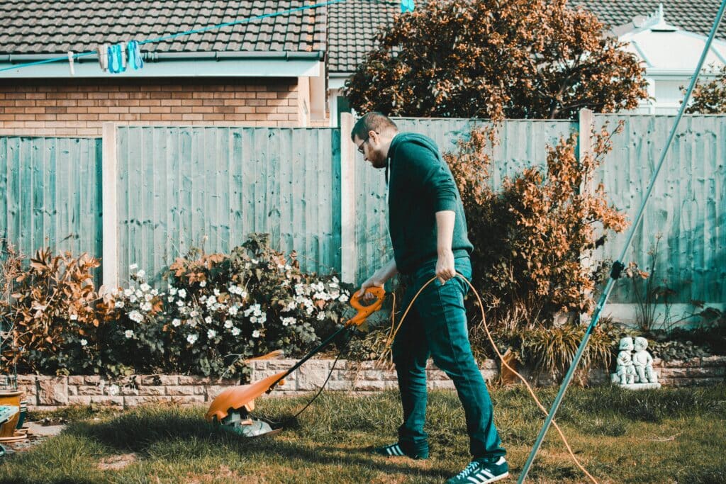 A man using an electric mower in a garden on a sunny day, capturing outdoor chores and gardening vibes.