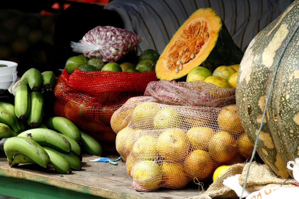 Vibrant display of fresh vegetables and fruits at a market stall, showcasing pumpkins, bananas, limes, and more.