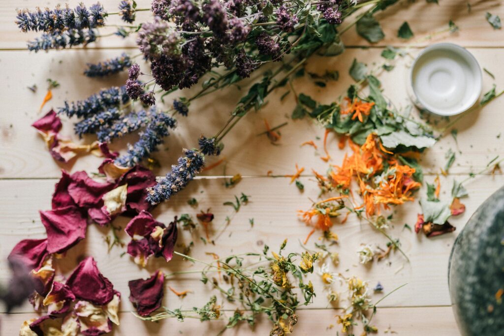 Assorted dried flowers and herbs scattered on a wooden table with a ceramic bowl.