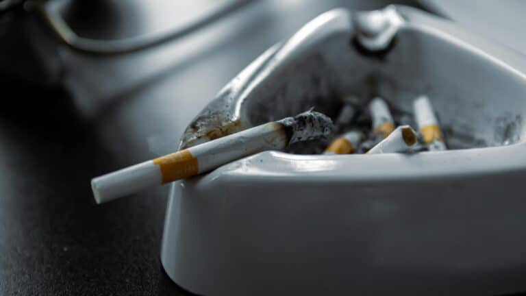 A close-up shot of a white ashtray filled with used cigarettes on a dark surface.